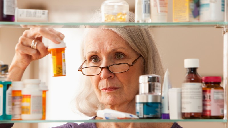 Older woman looking at pills in medicine cabinet  