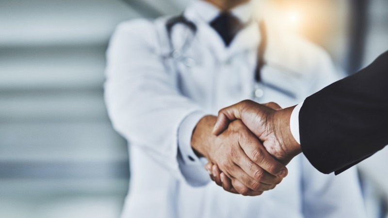 Closeup doctor shaking hands with another person in business suit