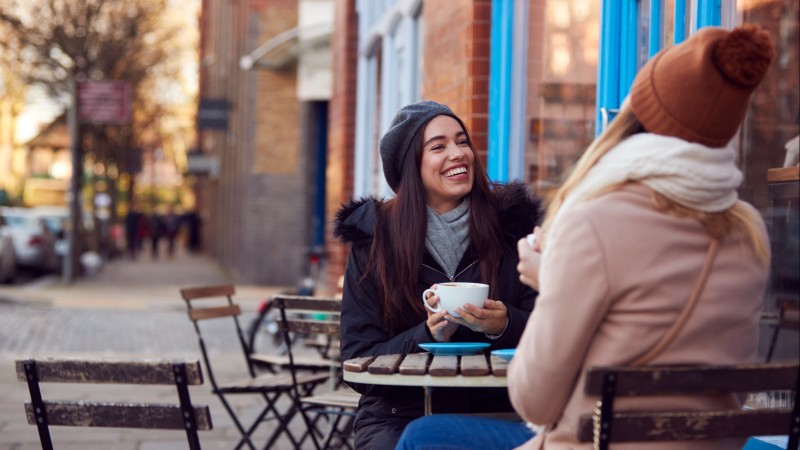 Two female friends have coffee at an outdoor cafe.