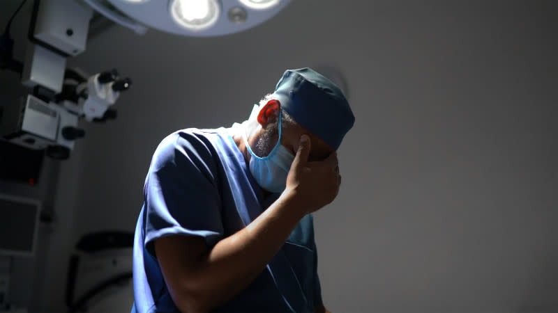 A distraught doctor puts his hand over his face.